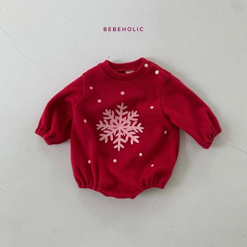 Ein roter Baby-Strampler mit langen Ärmeln und elastischen Bündchen, mit einem großen weißen Schneeflockenmuster in der Mitte und kleinen weißen Punkten, die darüber verstreut sind. Über dem Strampler steht das Wort „Star Bonnet Set“, was ihn perfekt für die himmlische Mode Ihres Kleinen von Bebe Holic macht.