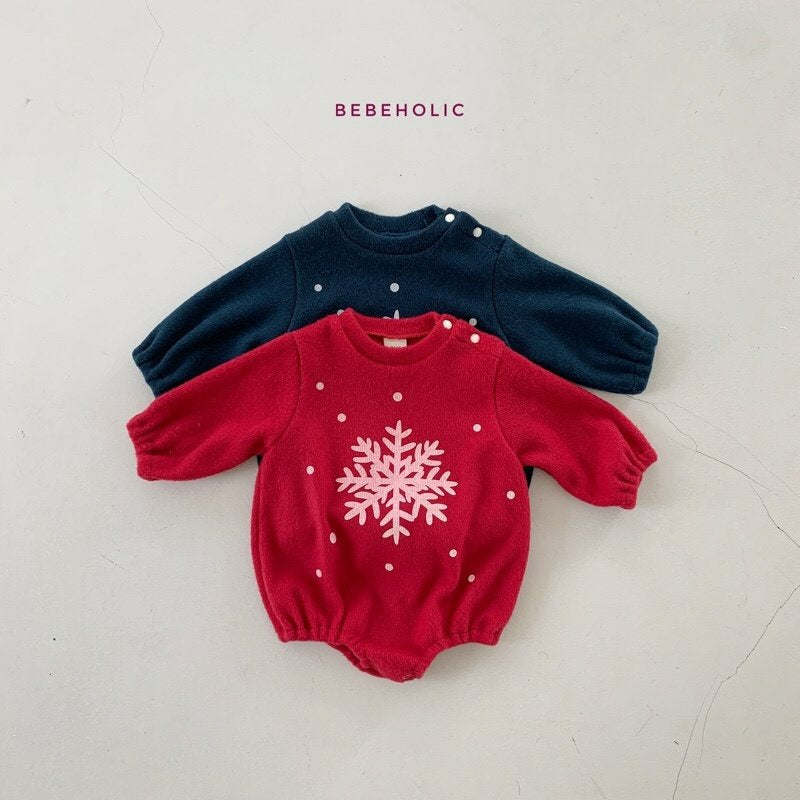 Zwei Strickpullover in Kindergröße liegen flach auf einem hellen Hintergrund. Der obere Pullover ist marineblau mit kleinen weißen Punkten. Der untere Pullover ist rot mit einem großen weißen Schneeflockenmuster und kleinen weißen Punkten. Oben ist der Markenname „Bebe Holic“ zu sehen, der die Star Bonnet Set-Kollektion präsentiert.