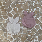 Zwei Lily Wing Body Suits auf einem Mosaikfliesenboden. Einer ist grau und der andere staubrosa, beide mit gerüschten Ärmeln und gerafftem Ausschnitt. Der Text „Bebe Holic Strampler