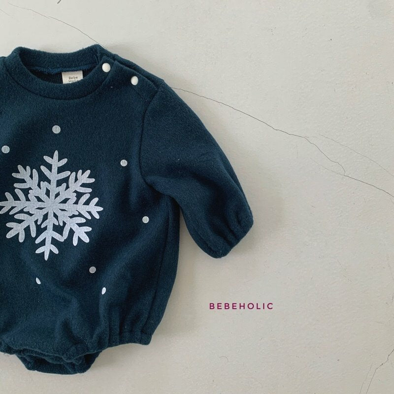 Ein dunkelgrüner Baby-Strampler mit einem weißen Schneeflockenmuster in der Mitte und weißen Punkten drumherum. Der Strampler hat lange Ärmel, Druckknöpfe an einer Schulter und unten ist in Pink „Bebe Holic“ aufgedruckt. Ergänzen Sie diesen Look mit unserem passenden Star Bonnet Set von Bebe Holic für einen Hauch himmlischer Mode auf dem hellen, rissigen Hintergrund.