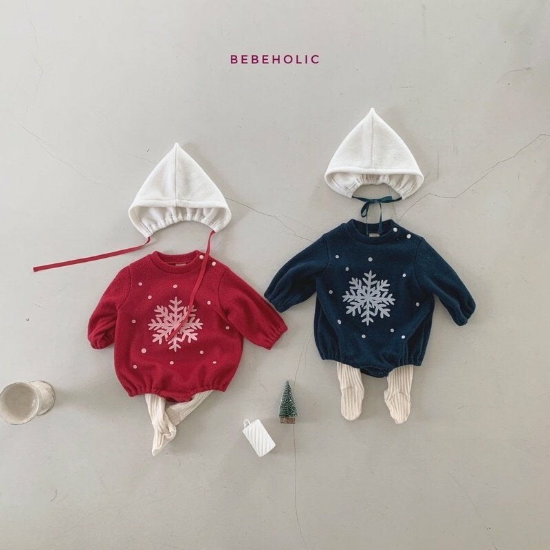 Zwei festliche Baby-Outfits liegen nebeneinander. Das linke Outfit aus der Kollektion von Himmlische Mode besteht aus einem roten Pullover mit weißem Schneeflockenmuster, cremefarbenen Strumpfhosen und einem Star Bonnet Set von Bebe Holic. Das rechte Outfit besteht aus einem marineblauen Pullover mit weißem Schneeflockenmuster, cremefarbenen Strumpfhosen und einer weißen Haube.
