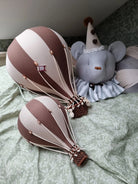 Zwei SuperBalloon - Bunte Luftballons für magische Kinderzimmer-Momente von Superballoon mit braunen und weißen Streifen ruhen auf einer hellgrünen geblümten Tagesdecke und verleihen einen Hauch kreativer Raumgestaltung. Eine große, ausgestopfte graue Maus in einem weiß-grauen Clownskostüm mit passendem Spitzhut sitzt im Hintergrund an der Wand.
